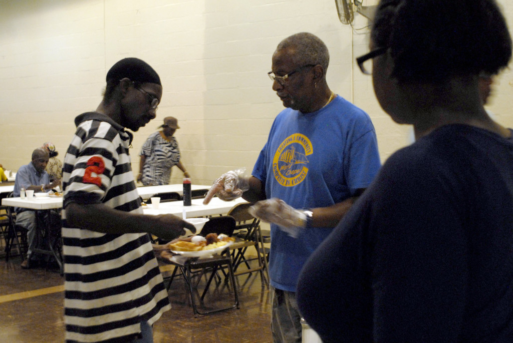 PHOTO BY CLARE HOWARD Cleo Carter asks a young man holding a bowl of grits if he wants some maple syrup. Carter grew up in Peoria near Mark Clark’s family. Clark was a member of the Black Panther Party when he started a breakfast program for children at Ward Chapel AME Church. 